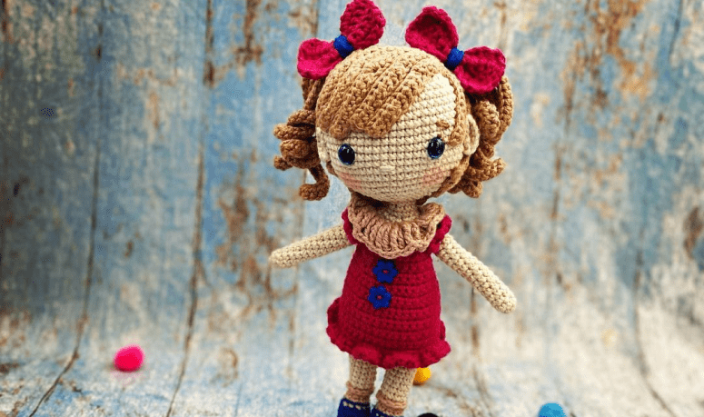 Uma boneca de crochê com uma roupa laranja nas folhas